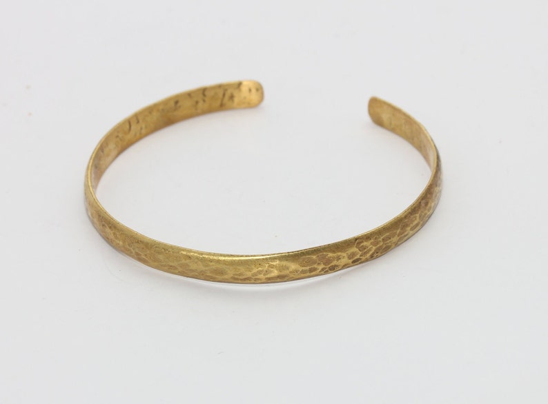 Puede incluir: Un brazalete de lat&oacute;n martillado. El brazalete abierto tiene una superficie texturizada y un color dorado c&aacute;lido. El brazalete es un dise&ntilde;o simple y elegante, adecuado para el uso diario.
