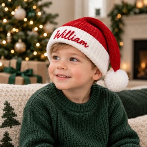Op de afbeelding: Een rood-witte gebreide kerstmuts met een witte geribbelde boord waarop de naam William in rode schrijfletters is geborduurd en een witte pompon aan de punt.