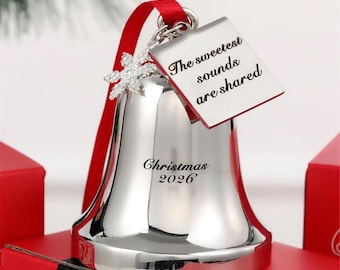 May include: A silver-toned bell ornament featuring a red ribbon, a snowflake charm, and a square tag engraved with the text The sweetest sounds are shared. The bell is inscribed with the text Christmas 2026 in a black serif font.