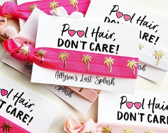 May include: Pink and white hair ties with gold palm tree designs and a white card with the text "Pool Hair, Don't Care!" and "Allyson's Last Splash".