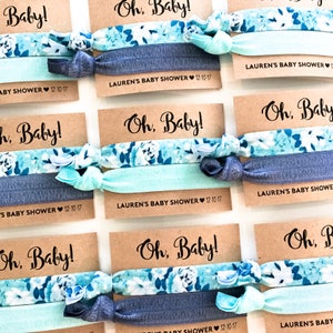 May include: Set of six blue and white floral hair ties with a brown card attached to each. The card reads "Oh, Baby!" and "Lauren's Baby Shower 12-10-17".