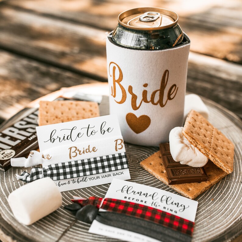 以下が含まれることがあります： 白い缶クーラーに金色の文字で「Bride」と書かれたもの、黒と白のチェック柄のヘアゴムに「bride to be Bride B three & to hold YOUR HAIR BACK」という文字が書かれたもの、赤と黒のチェック柄のヘアゴムに「flannel bling BEFORE the RING」という文字が書かれたもの、これら3点のブライダルシャワーパーティーのお土産セットです。