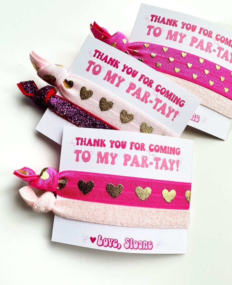Pode incluir: Cart&otilde;es de lembrancinhas de festa com el&aacute;sticos de cabelo. Os cart&otilde;es dizem "THANK YOU FOR COMING TO MY PAR-TAY!" em rosa. Os el&aacute;sticos de cabelo s&atilde;o rosa, dourado e roxo brilhante, com detalhes de cora&ccedil;&atilde;o dourado. O cart&atilde;o inferior diz "Love, Sloane".