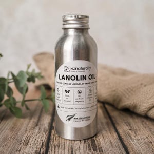 May include: A silver metal bottle of Lanolin Oil with a white label. The label reads "nz naturally" and "LANOLIN OIL". The bottle is on a wooden surface. The label also states "100% All Natural" and "No artificial fragrance".
