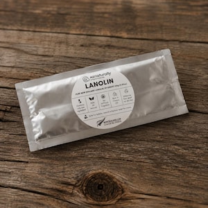 May include: A silver packet of "LANOLIN" from nz naturally, containing 100g of pure New Zealand lanolin. The product label is white with black text and icons. The packet is on a wooden surface.