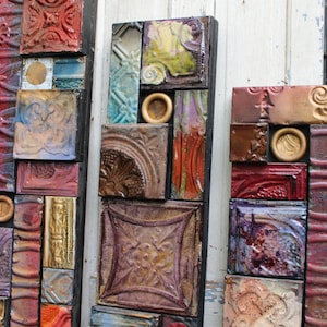 May include: Three vertical wall art pieces made of various colored and patterned tiles. The tiles are arranged in a random pattern and are framed in black.