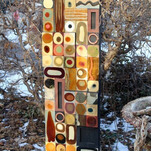 May include: A rectangular wall art piece made of colorful tiles. The tiles are arranged in a geometric pattern with circles, squares, and rectangles. The colors are mostly brown, orange, yellow, and white.