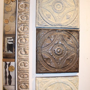 Puede incluir: Cuatro tejas de techo decorativas de estaño con diseños intrincados. Las tejas son de varios tonos de marrón y blanco, con un diseño central en relieve. Las tejas están dispuestas verticalmente en una pared blanca.