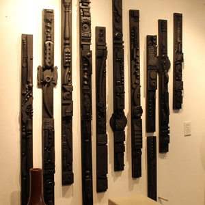 Peut inclure: Une exposition murale de 10 sculptures en bois noir, chacune avec un design géométrique unique. Les sculptures sont disposées en ligne verticale, la plus haute à gauche et la plus courte à droite. Les sculptures sont toutes faites du même type de bois et ont une finition lisse et polie.