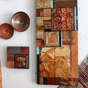 Puede incluir: Una pieza de arte de pared rectangular hecha de varios azulejos en tonos marrones, dorados y azules. Los azulejos están dispuestos en un patrón de mosaico y tienen un aspecto rústico y vintage.