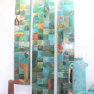 Op de afbeelding: Drie verticale wandkunstwerken met een mozaïekontwerp van kleine, vierkante tegels in tinten turquoise, groen en oranje. Een bruine vaas en een turquoise keramische vaas met handvatten staan op de voorgrond. Een turquoise doek en een decoratieve bal zijn ook zichtbaar.