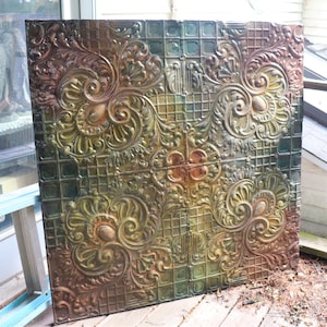 May include: A vintage tin ceiling tile with a decorative, ornate design in shades of green, gold, and brown. The tile has a raised, embossed pattern.