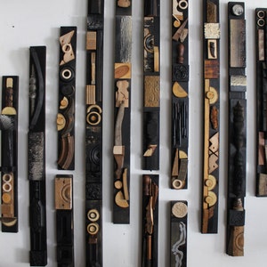 May include: A collection of ten vertical wall art panels, each featuring a black rectangular base adorned with an assortment of small, varied wooden shapes, textured elements, and geometric pieces in natural wood tones, black, and metallic finishes.