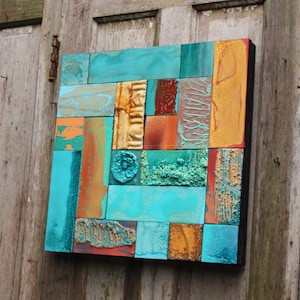 May include: A square abstract art piece made of wood tiles. The tiles are painted in shades of turquoise, gold, orange, and brown. The tiles are arranged in a geometric pattern.