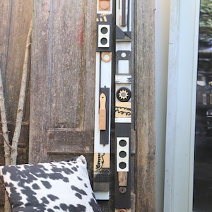 Peut inclure: Une sculpture abstraite haute en bois peinte en noir, blanc et marron. La sculpture est composée de différentes formes géométriques et motifs. Elle est appuyée contre une porte en bois et une porte blanche.