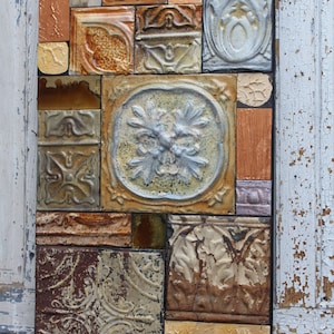 May include: A wall art piece made of various vintage tiles in shades of brown, beige, and gray. The tiles feature intricate floral and geometric patterns.