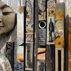 May include: A wall art piece made of various materials, including wood, metal, and ceramic. The piece features a variety of textures and colors, including brown, black, white, and yellow. The piece is arranged in a vertical pattern, with the different materials and colors creating a visually interesting and abstract design.