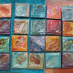 May include: Twenty-four ceramic tiles with a leaf design in various shades of blue, green, orange, and brown. The tiles are arranged in four rows of six tiles each.