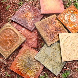 May include: Nine decorative ceramic tiles with intricate designs in shades of brown, orange, and gold. The tiles have a raised, textured surface and are arranged in a random pattern.