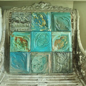May include: A vintage cast iron bench with a decorative back featuring a mosaic of nine turquoise and green tiles. The tiles have a floral design and are arranged in a grid pattern.