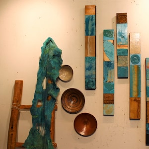 May include: A wall display of six vertical wooden panels with a blue and brown mosaic design. The panels are arranged in a staggered pattern. There is a wooden ladder, a teal fabric, and three bowls on the wall.