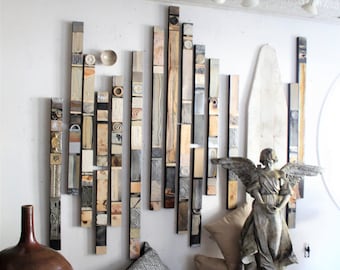 May include: A decorative wall art installation composed of vertical wooden planks in various colors and textures. A bronze angel statue, pillows, and a large brown vase are in the foreground. The ceiling has a white, ornate pattern.