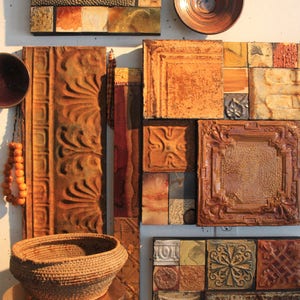 May include: A wall art piece made of various tiles in shades of brown, orange, and yellow. The tiles are arranged in a geometric pattern and have a rustic, vintage look. Some of the tiles have a raised design, while others are smooth. The piece is framed by a wooden border.