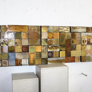 May include: A wall art piece made of small, square tiles in various shades of brown, beige, and gold. The tiles are arranged in a random pattern, creating a textured and abstract design.