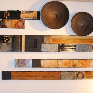 May include: A wall art piece made of various tiles and wood. The tiles are in different colors, shapes, and textures. The wood is a dark brown color. The art piece is arranged in a horizontal pattern.