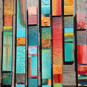 Può includere: Un'opera d'arte murale realizzata con diverse strisce di legno colorate, disposte verticalmente in un motivo a mosaico. Le strisce sono dipinte in tonalità di blu, verde, rosso, arancione e marrone.