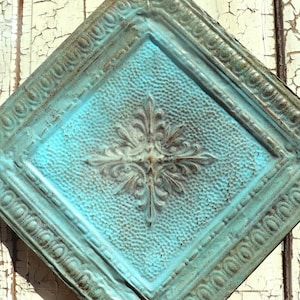 May include: A turquoise blue metal ceiling tile with an ornate, embossed design in the centre. The tile has a distressed, aged look.