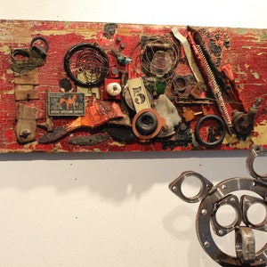 Puede incluir: Un panel de madera rojo con una variedad de objetos unidos a él, incluyendo piezas de metal, alambre y un pequeño trozo de papel con el número "5" en él.