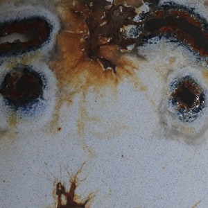 May include: Close-up of a weathered, off-white surface with dark brown and rust-colored markings. The surface has several oval-shaped, dark brown holes and a textured appearance, suggesting age and wear.