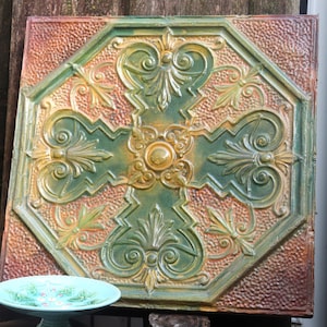 May include: A decorative ceiling tile with an intricate design featuring a cross shape with floral motifs. The tile is painted in shades of green, gold, and brown, creating a vintage aesthetic.