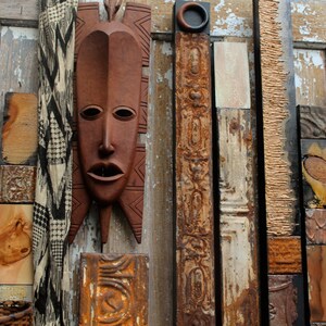 Könnte beinhalten: Ein Wandkunstwerk aus Holz mit verschiedenen Texturen und Farben. Das Stück zeigt eine geschnitzte Holzmaske mit brauner Oberfläche sowie verschiedene Holz- und Metallteile.