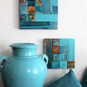 May include: Two square wall art pieces made of wood with a mosaic of blue, teal, and brown squares. A large teal ceramic vase sits in front of the art pieces.