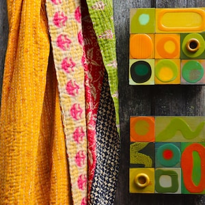 Könnte beinhalten: Zwei farbenfrohe abstrakte geometrische Kunstwerke mit einem Farbschema aus Gelb, Grün, Orange und Schwarz. Die Kunstwerke sind auf einer Holzoberfläche montiert.