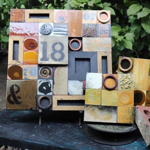 May include: A mosaic artwork made of ceramic tiles in various shades of brown, yellow, and white. The artwork features the number "18" and an ampersand symbol. The tiles are arranged in a grid pattern and have a rustic, handmade look.