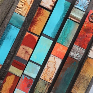 May include: A wall art piece made of wood and various colored tiles. The tiles are arranged in a diagonal pattern and feature shades of blue, green, orange, and brown.