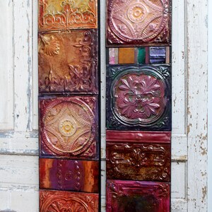 May include: Two vertical wall decor pieces made of colorful, patterned tin tiles. The tiles are arranged in a vertical stack and feature a variety of geometric and floral designs. The tiles are in shades of red, orange, yellow, green, blue, and purple.