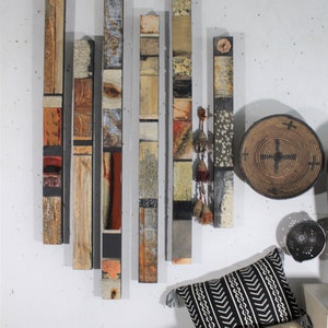 Puede incluir: Una pieza de arte de pared hecha de madera con cuadrados de diferentes colores y texturas. La pieza está compuesta por siete paneles verticales, cada uno con un patrón diferente. Los paneles están dispuestos en un patrón escalonado, creando un efecto visual dinámico e interesante.
