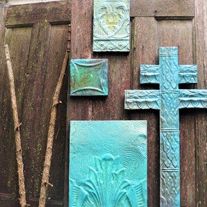 May include: A wooden door with a cross-shaped design and four square tiles with a blue and green patina. The tiles have a raised design and are arranged in a symmetrical pattern.