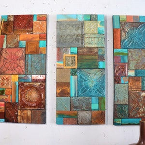 Op de afbeelding: Drie rechthoekige wanddecoraties gemaakt van hergebruikte tegels in tinten bruin, blauw, groen en oranje. De tegels zijn in een patchwork-patroon gerangschikt.