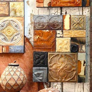 Könnte beinhalten: Eine Ansammlung dekorativer Metallfliesen in verschiedenen Formen, Farben und Texturen. Die Fliesen sind an einer Wand angeordnet und zeigen eine Mischung aus geprägten Mustern und gealterten Oberflächen. Ein geflochtener Korb mit Deckel befindet sich im Vordergrund.