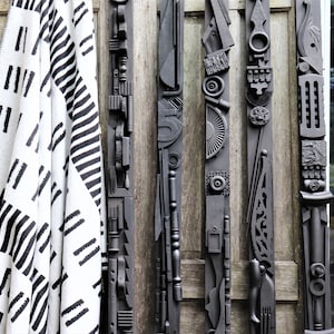 Può includere: Cinque sculture in legno nero con disegni astratti, appese a una parete di legno. Le sculture sono realizzate con diversi materiali, tra cui legno, metallo e plastica.