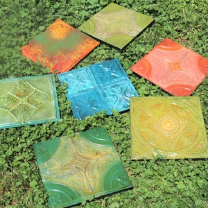May include: Six decorative tin ceiling tiles in various colors and patterns, including green, blue, yellow, and orange. The tiles are arranged on a bed of green grass.