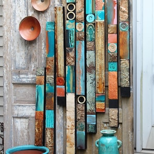 May include: A wall art piece made of wood and tile with a mix of turquoise, blue, brown, and orange colors. The art is displayed on a weathered wooden door with two turquoise ceramic pots and a vase.