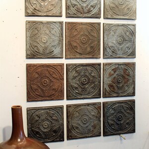May include: A grid of twelve square metal ceiling tiles arranged in four rows and three columns. Each tile features a raised, embossed circular pattern with intricate floral and geometric details in shades of weathered gray, brown, and rust.