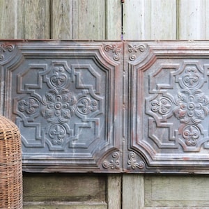 Puede incluir: Dos paneles de pared decorativos de metal con un diseño elevado y ornamentado. Los paneles son de color gris claro con un toque de óxido. Los paneles están montados en una pared de madera.