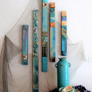 Könnte beinhalten: Fünf vertikale Holzpaneele mit einem Mosaik aus blauen, grünen und braunen Fliesen. Die Paneele sind in einer Reihe an einer weißen Wand angeordnet. Eine blaue Vase und ein Netz befinden sich im Vordergrund.